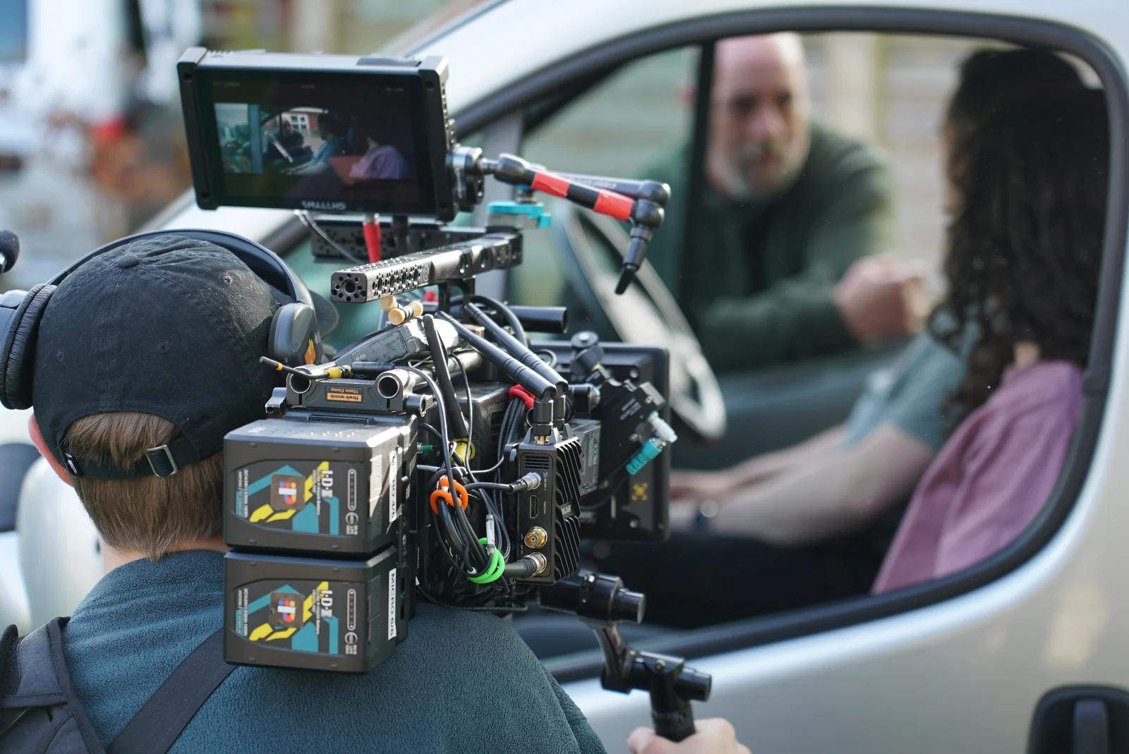 A camera operator filming through a car window