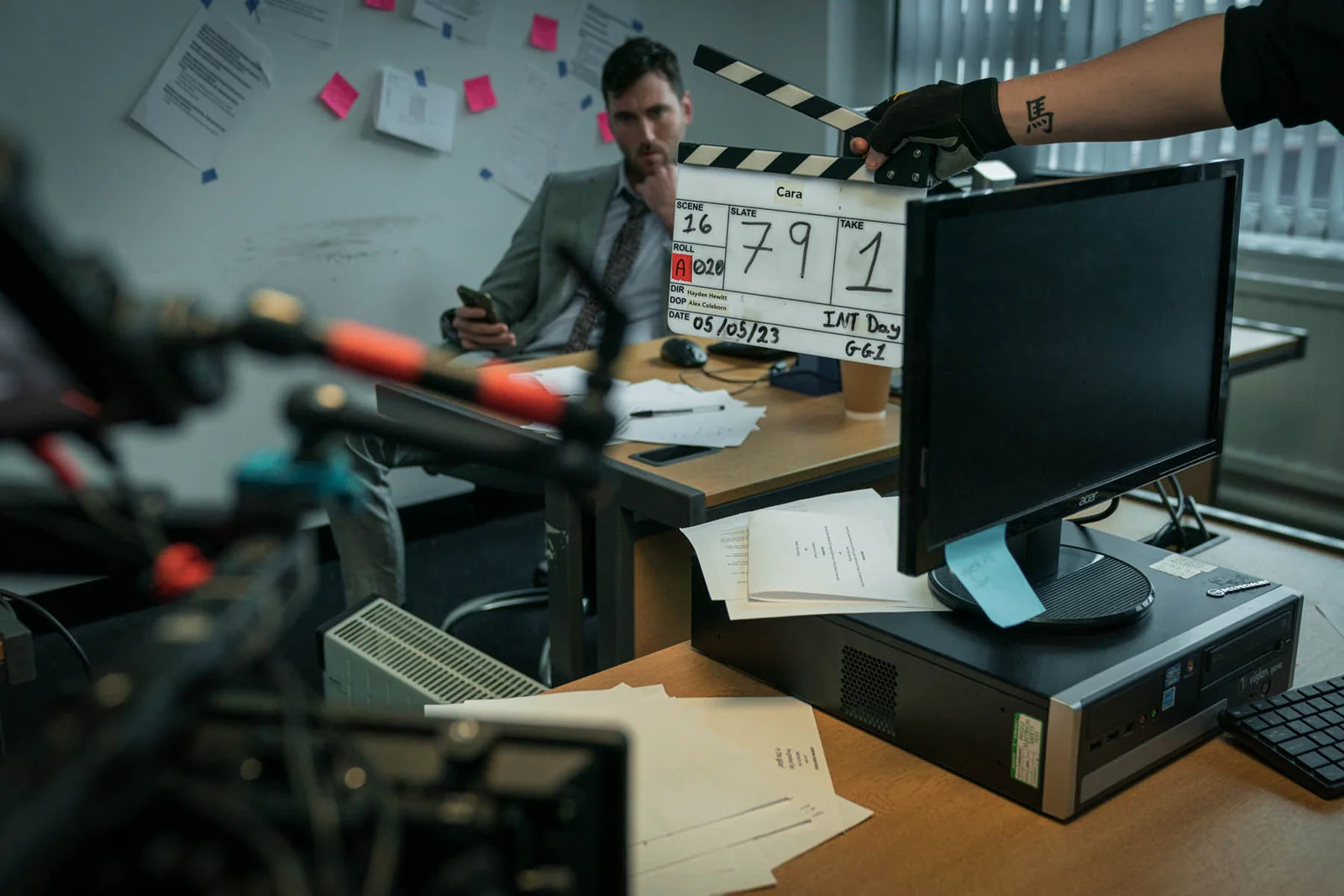 A clapperboard held in front of the office scene